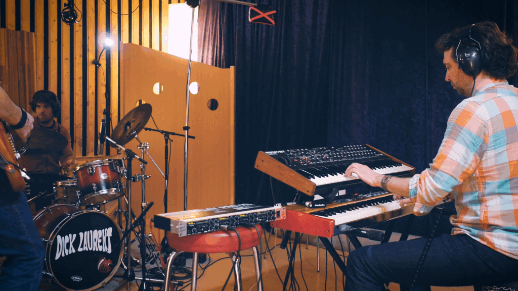 The hand of a guitar payer, a drummer drumming, and a keyboard player recording in studio. (Dick Laurent recording EP "Melted")